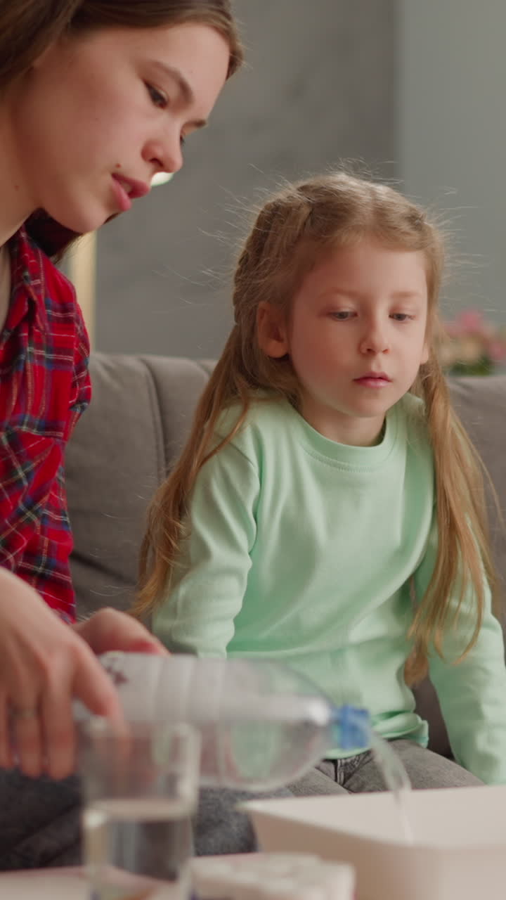 niña con camisa a cuadros roja vierte agua en la bandeja para enseñar a la hermana pequeña ebru a dibujar en la mesa en la sala de estar. afición artística familiar. afición creativa y ocio