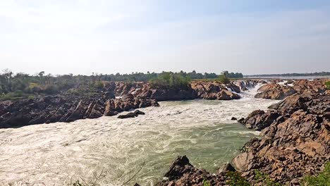 a dynamic view of waterfalls in champasak, laos, under bright daylight. the camera captures the powerful water flow and rocky landscape