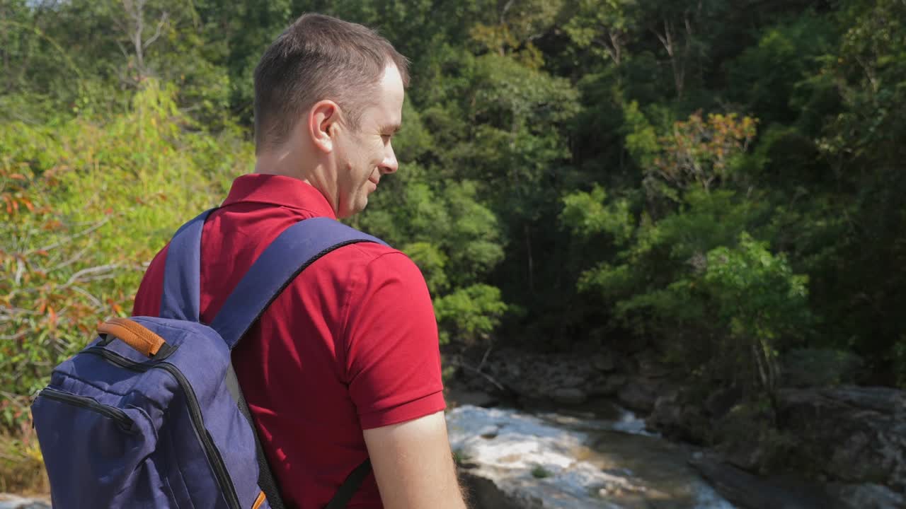 바위 강 근처 에 서 있는 배 과 함께 빨간 폴로 셔츠 를 입은 여행자