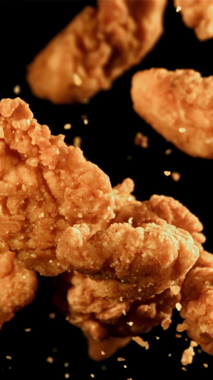 Nuggets de pollo fritos crujientes cayendo a cámara lenta sobre fondo negro