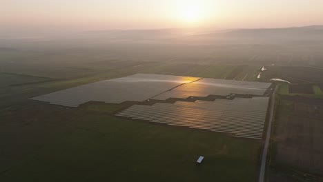 solar panels in a vast green field during a misty sunrise, aerial view