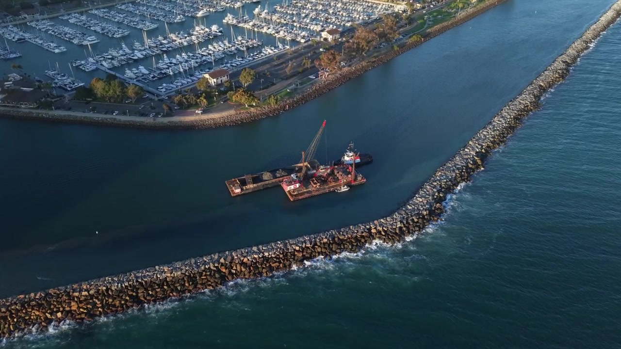 Aerial zoom toward the Dredging Barge in the Harbor from high above the sea. Beautiful Blue waters surround the Barge at Sunset as the harbor lights begin to turn on.