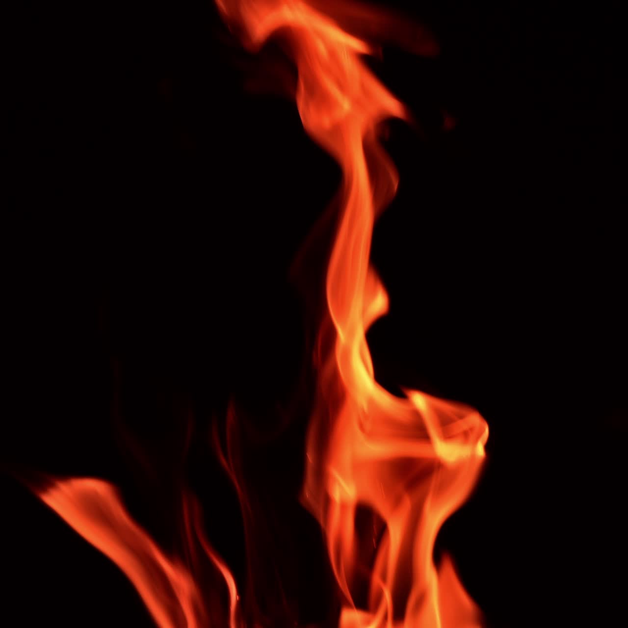 Dancing fire flames in total darkness. Tongues of blaze swaying to and fro and tiny sparkles flaring at night