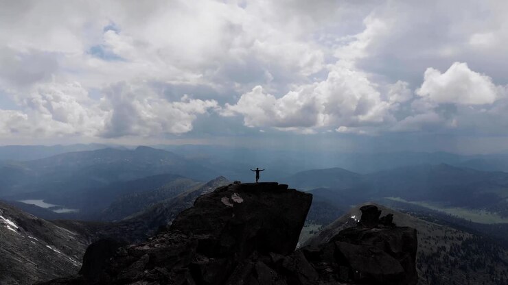 Un uomo si erge sulla cima di una montagna.
