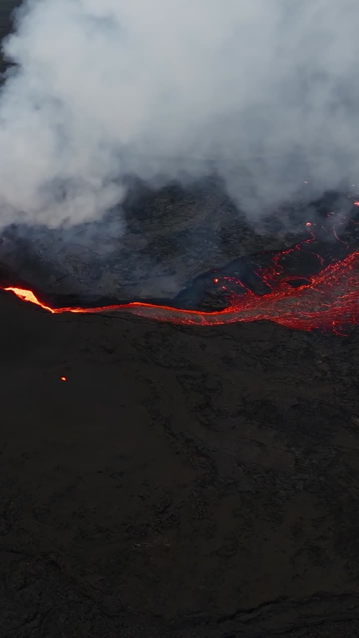 Thick cloud of smoke spreading over the active vent and flowing bright lava. Aerial drone overview