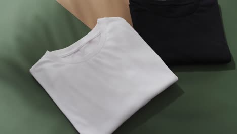 Video-of-flat-lay-of-folded-white-and-black-t-shirts-with-copy-space-on-green-and-brown-background