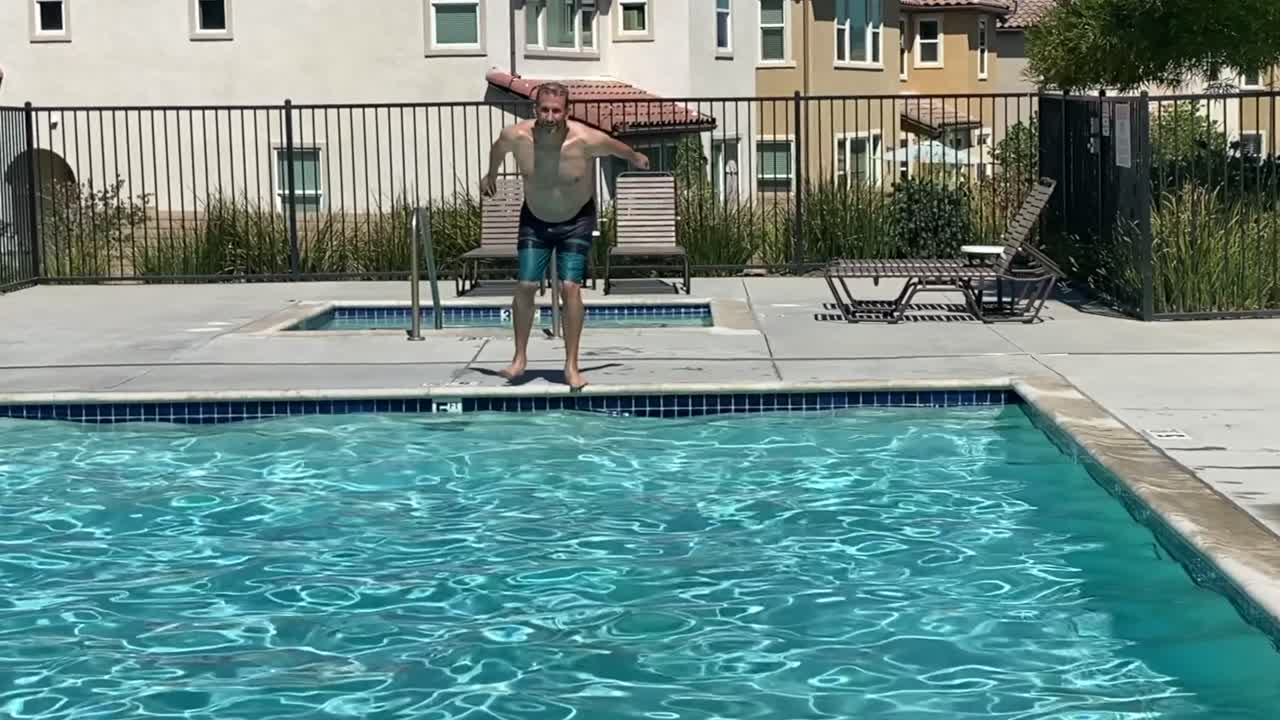 hombre caucásico saltando a la piscina de la comunidad en un día caluroso de verano