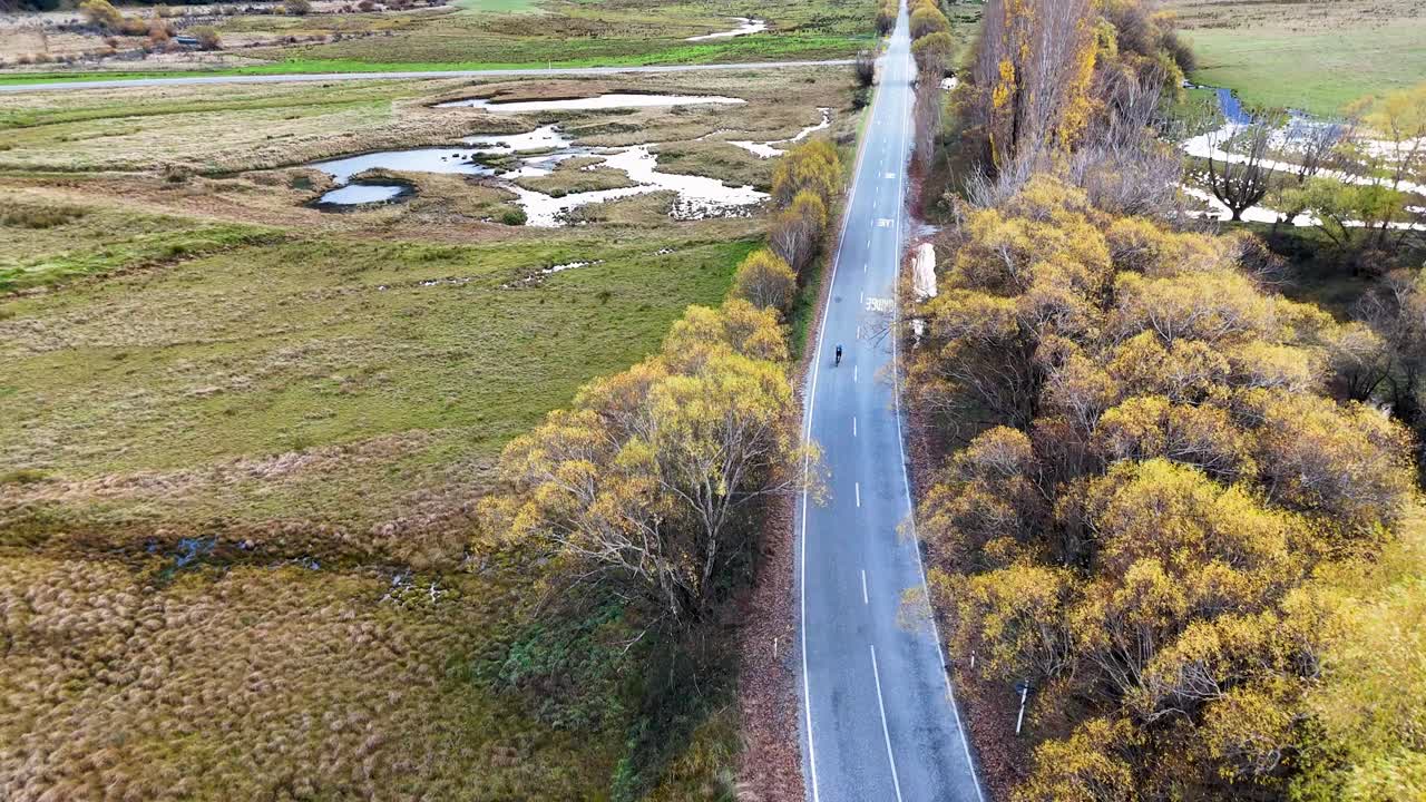 Aerial view of a winding road through lush greenery and fields in Glenorchy, New Zealand, under soft natural lighting