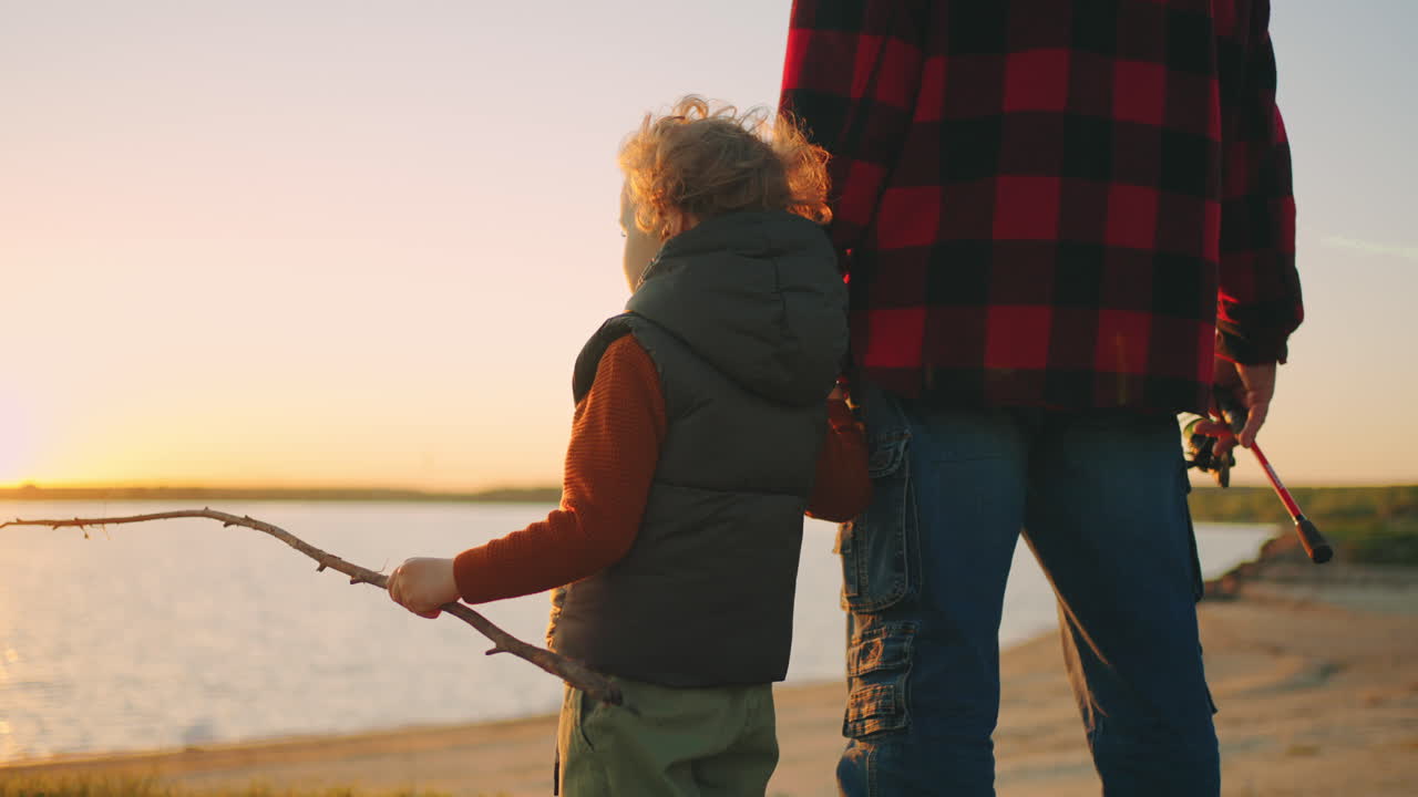 little boy is holding hand of father and admiring beautiful landscape with river and sunset