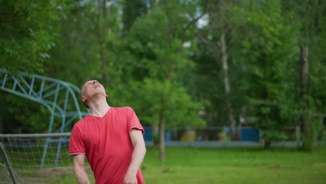 a man in a red shirt taps a soccer ball high and skillfully heads it away as it descends, close to a goal post in a grassy field