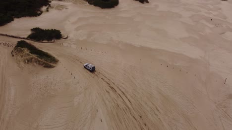 high aerial following shot of the four wheel car leaving beach and driving on rural forest road beside the beach water waves in south america , argentina