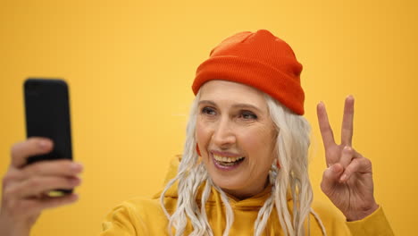 Joyful-old-woman-posing-hone-camera-in-studio.-Happy-lady-making-selfie-indoors.