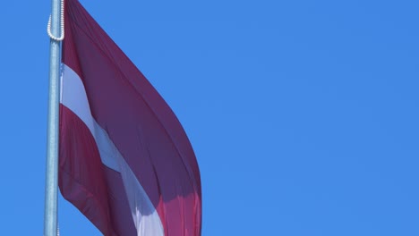 Large-Latvian-flag-waving-slow-on-blue-sky-in-sunny-day,-close-up-shot