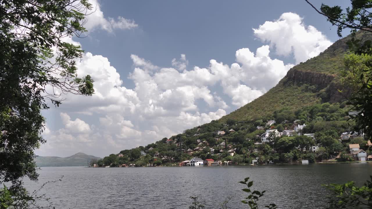 presa de hartbeespoort enmarcada por ramas de árboles, laderas de montañas, cielo nuboso