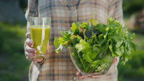 a woman holds a glass of green smoothie and a plate of lettuce