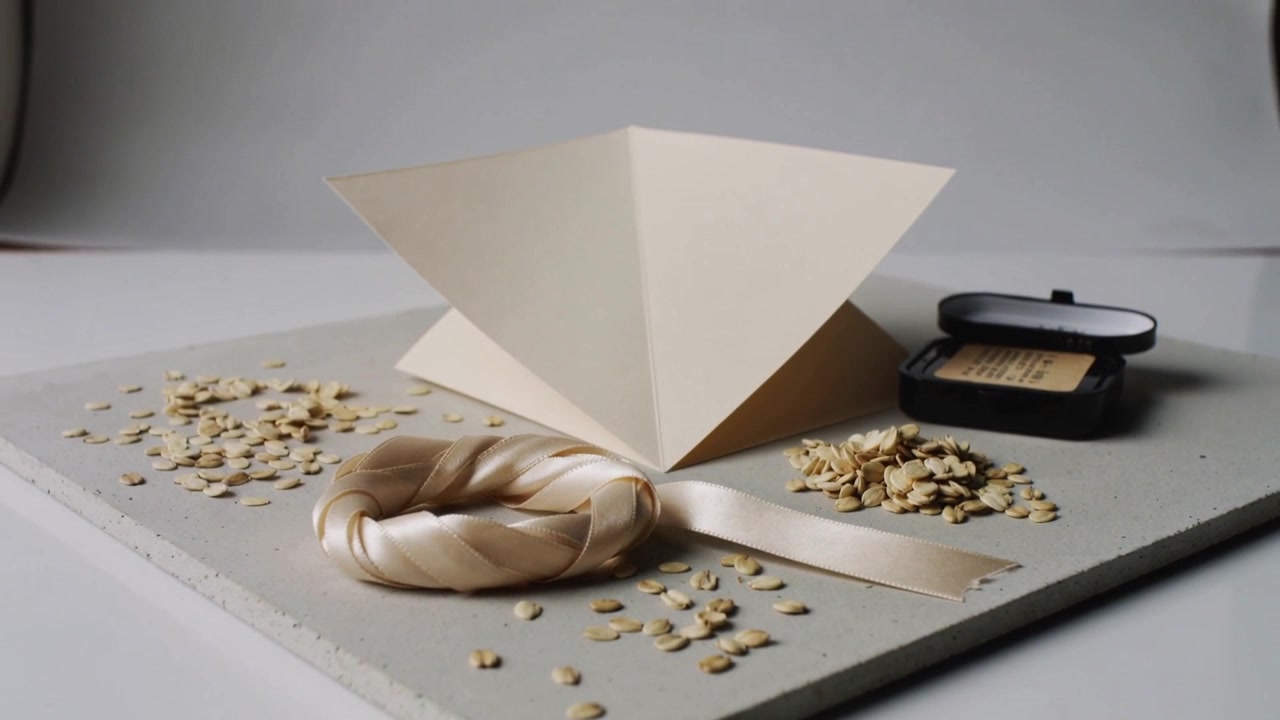 La telecamera si allontana rivelando un set da tavolo da studio che mostra un nastro di raso, una piramide di carta, scaglie e un fondotinta compatto.