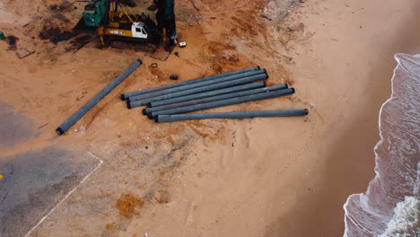 aerial top down of a crane parked in tropical vietnamese sandy beach pipes ready for installation on the natural seascape