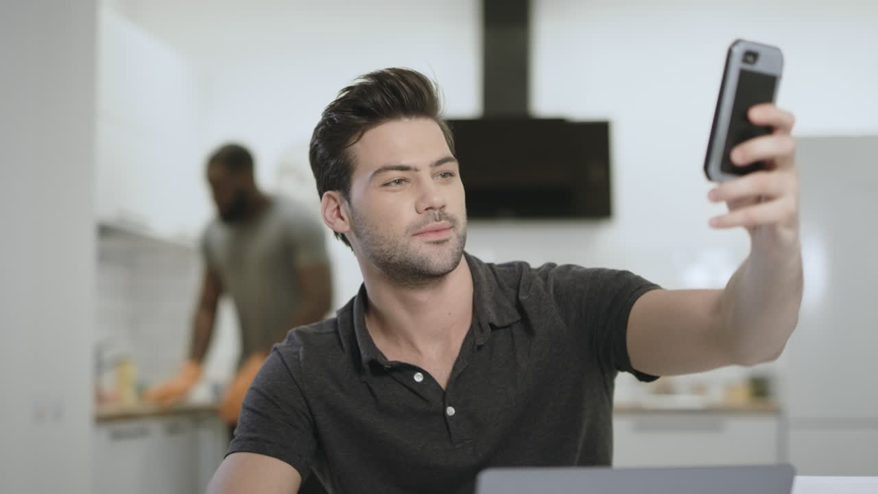 오픈 키친에서 셀카를 찍는 진지한 남자,  ⁇ 드폰을 들고 있는 젊은 남자