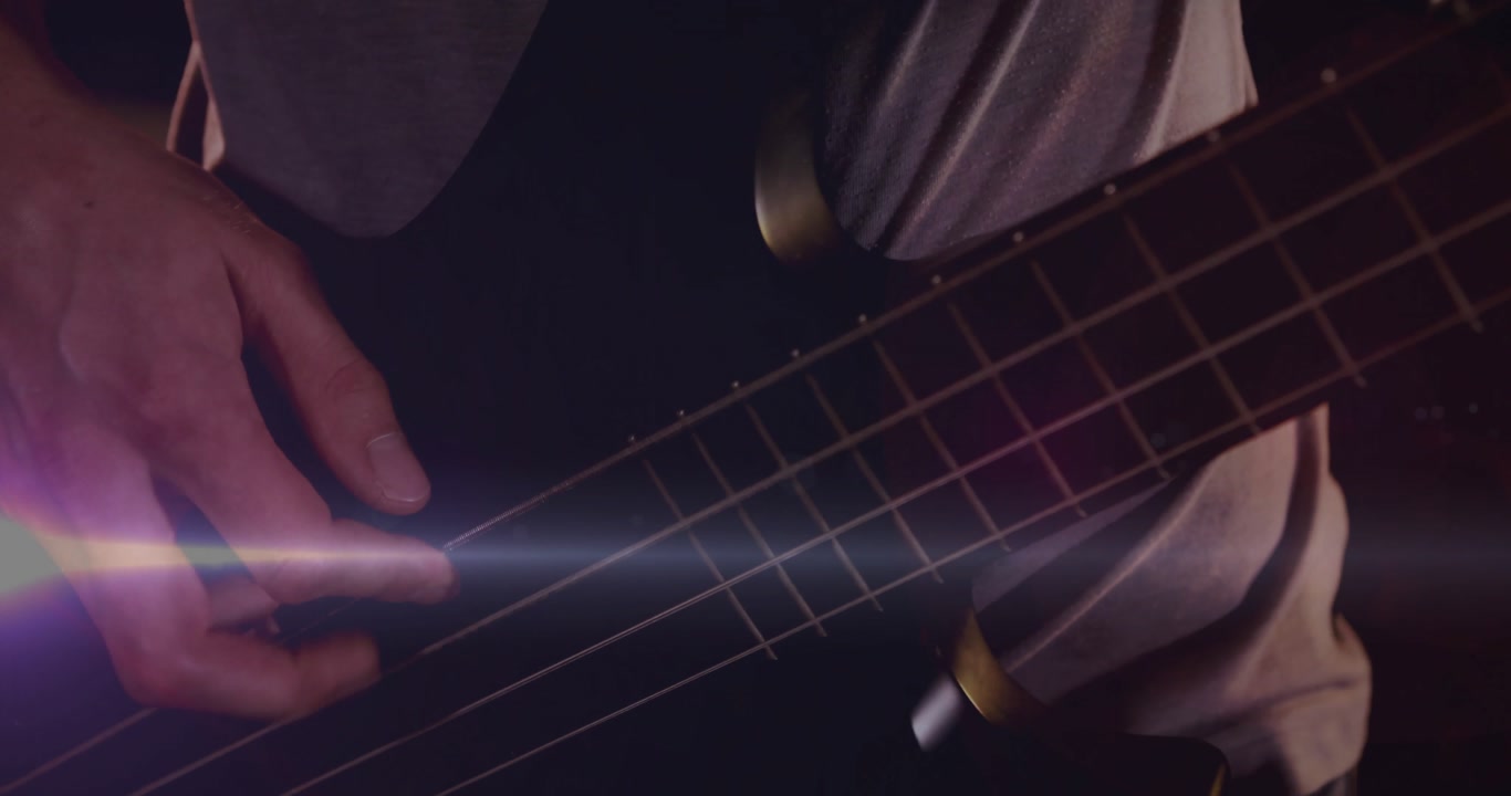 Bassist plucking four bass strings as camera panning triggers lens flare highlighting music groove