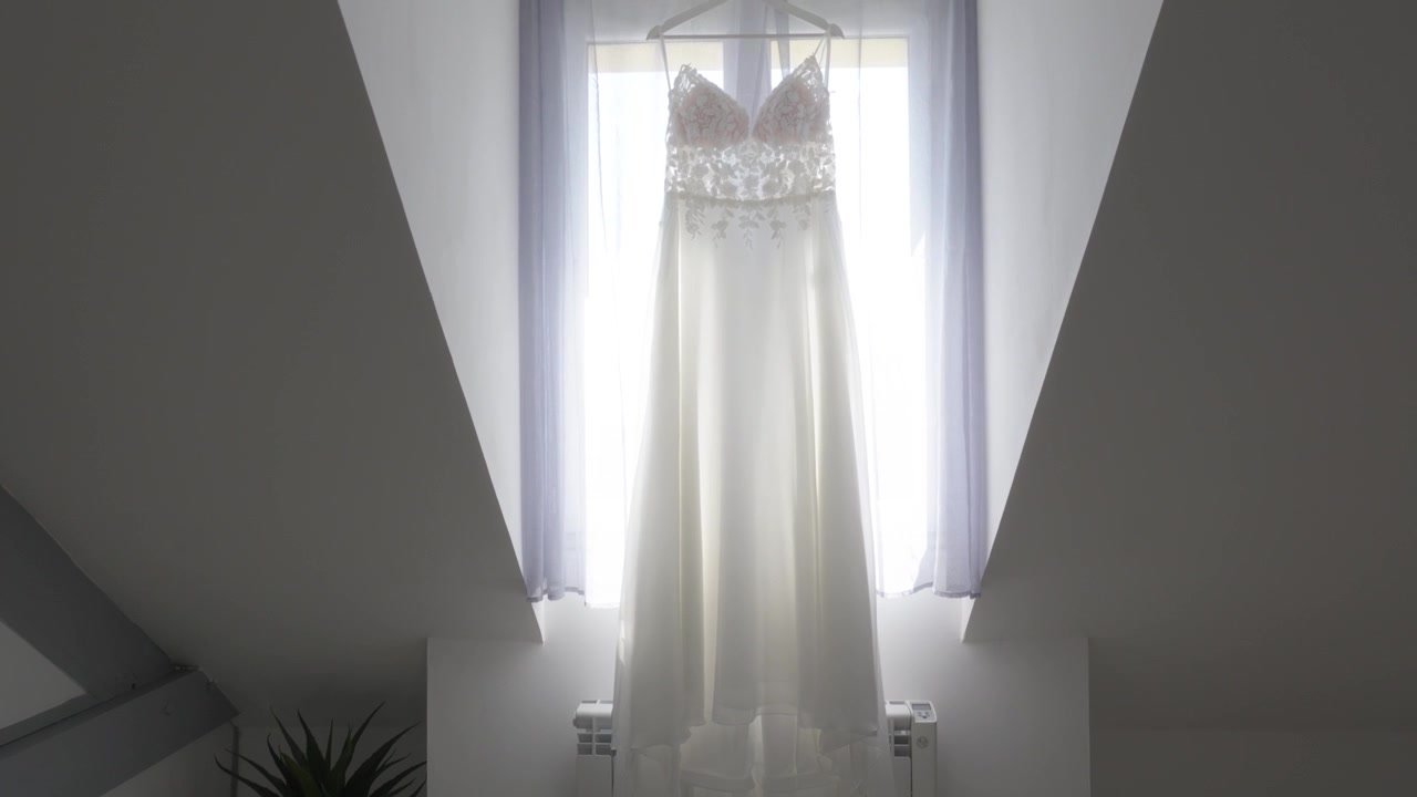 Abito da sposa appeso sotto una finestra luminosa con scarpe da sposa in una stanza minimalista.
