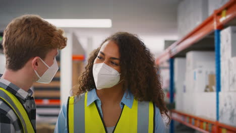 female team leader in warehouse training male intern standing by shelves both wearing face masks