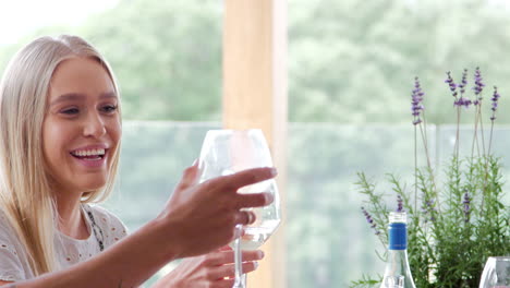 Four-young-adult-friends-celebrate,-smiling-and-raising-wine-glasses-during-a-dinner-party,-panning-shot,-close-up