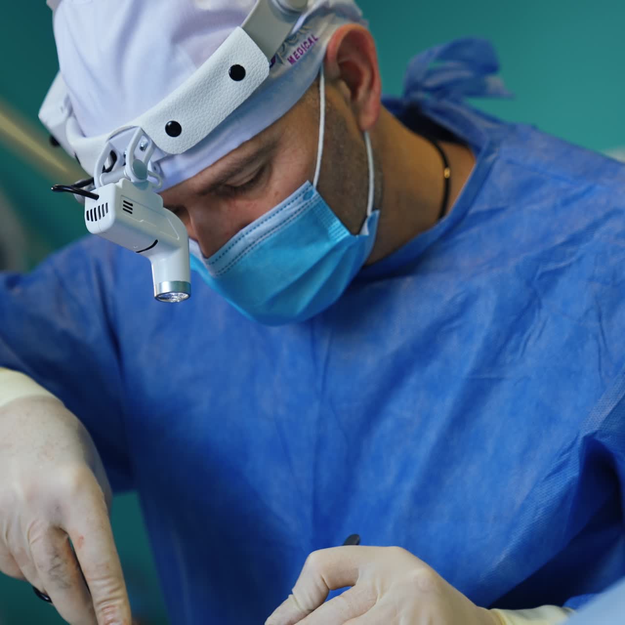 Focused busy surgeon with flashlight on head applying metal tools. Portrait of a medical professional carrying out surgery