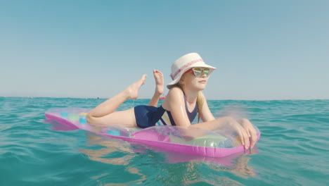 Ein-Mädchen-Mit-Hut-Und-Sonnenbrille-Schwimmt-Im-Meer-Auf-Einer-Aufblasbaren-Matratze-Frohes-Urlaubskonzept