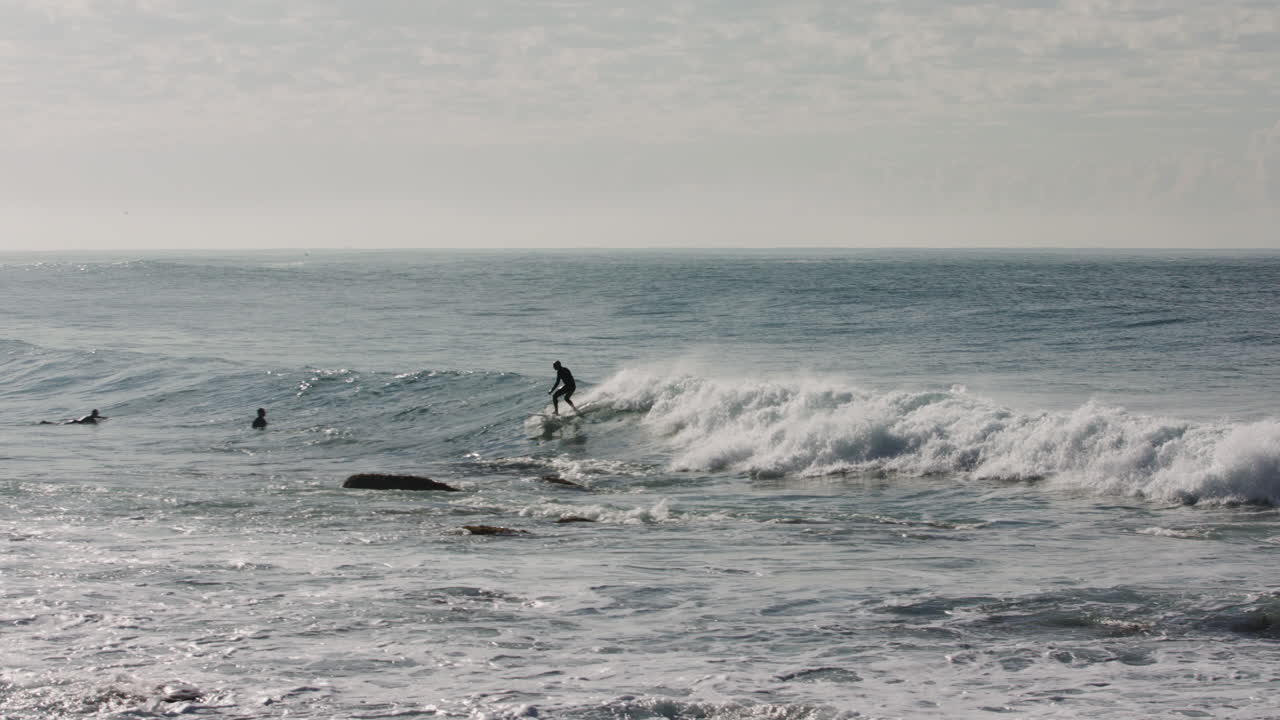 Un surfista ha tagliato un'onda evitando un gruppo di rocce che spuntavano dall'Oceano Pacifico con la bassa marea