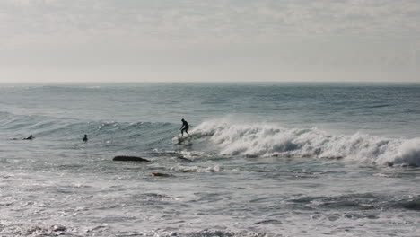 a surfer cut across away wave while avoiding a patch of rocks sticking out of the pacific ocean at low tide