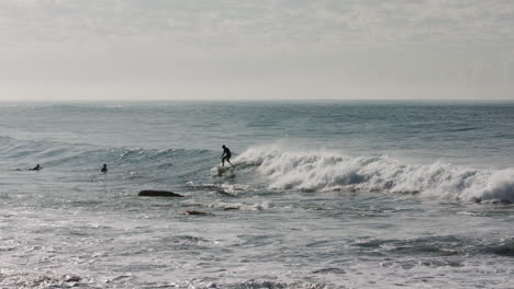 A surfer cut across away wave while avoiding a patch of rocks sticking out of the Pacific ocean at low tide