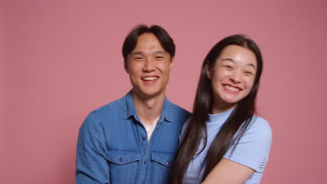 분홍색 스튜디오 배경 앞의 젊은 사랑하는 커플이 사진 부스 스타일의 초상화를 위해 포즈를 취하고 있습니다.