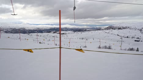 Moving-sideways-showing-fence-and-ski-lift-with-no-people-in-very-windy-weather-at-mountain-top---Ski-destination-Norway