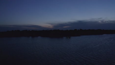 aerial reverse shot with boat on lake passing by during twilight