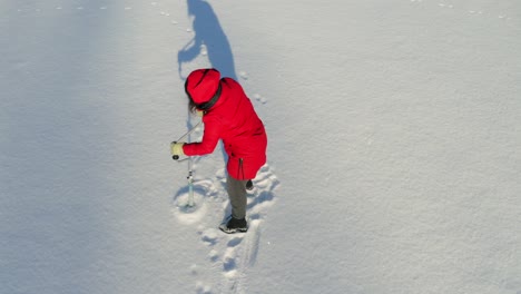 girl in red hooded jacket drill hole on snowy ground using an ice fishing auger - high-angle shot