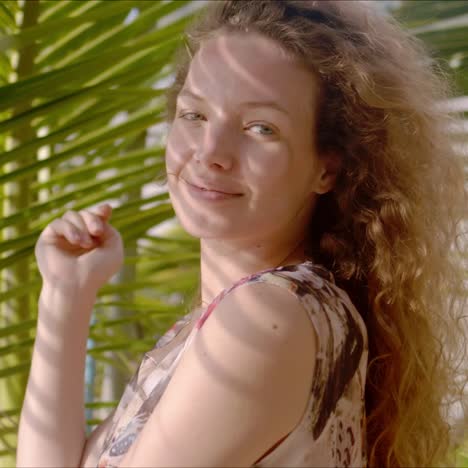 Smiling-lady-standing-in-shade-of-palm-leaves