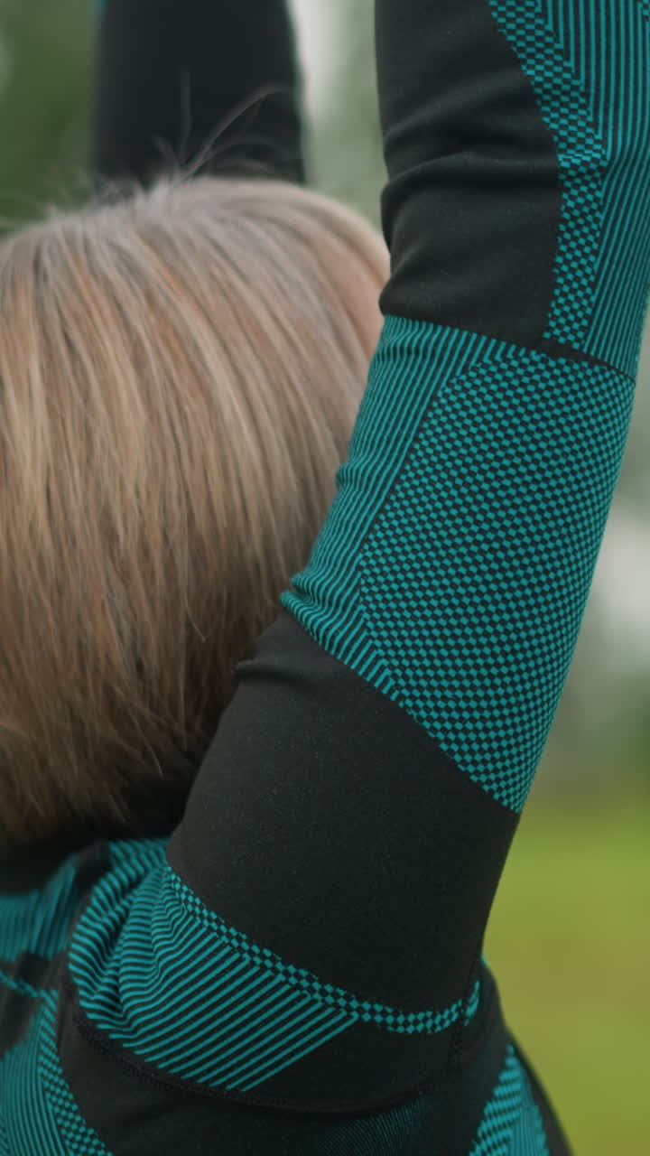 Side view of middle-aged woman raising arms and bringing hands together in meditation, practicing mindfulness outdoors in a grassy misty field under a cloudy sky