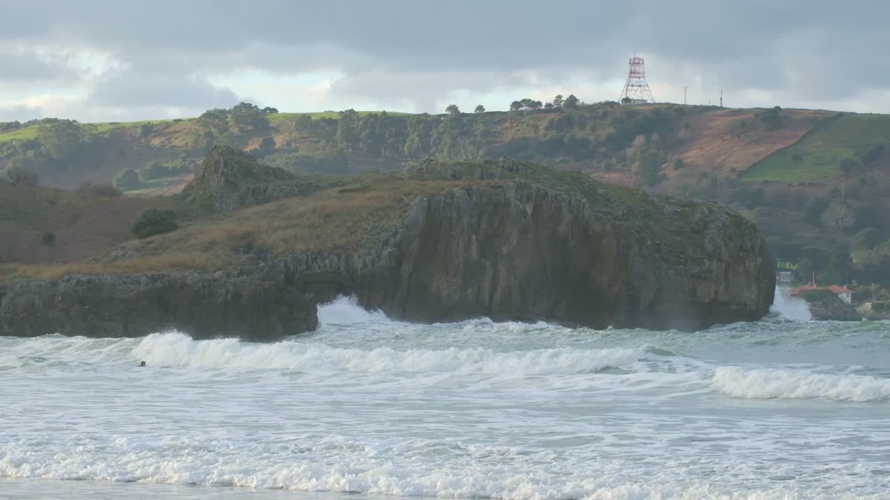 Panoramic view of large waves and an antenna on a cloudy day