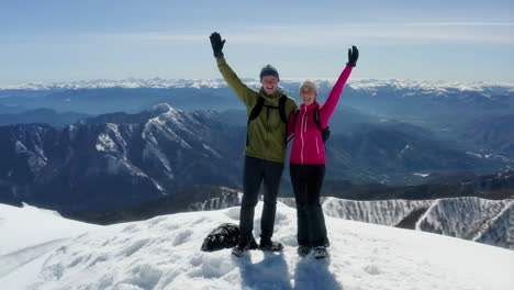 two happy hikers celebrate on a snowy mountain peak