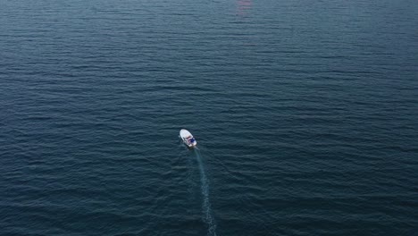 a small white dory makes a slight zag crossing deep open water, aerial