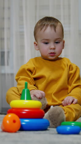 adorable little baby in orange suit sits surrounded by toys. cute child looks aside and pulls his sock from a foot. vertical video
