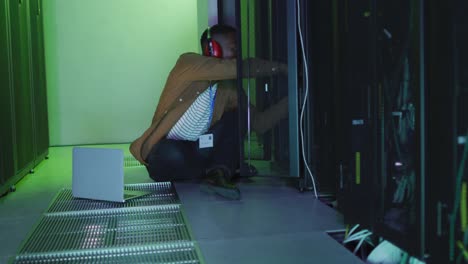 african american male computer technician using laptop working in business server room