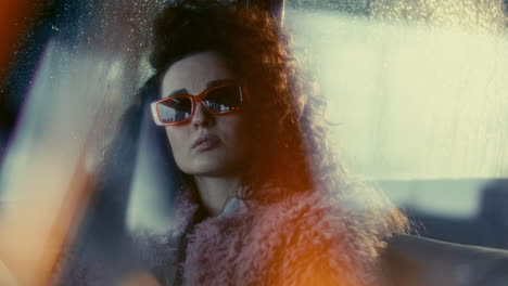 portrait of beautiful woman in sunglasses sitting in car on rainy night