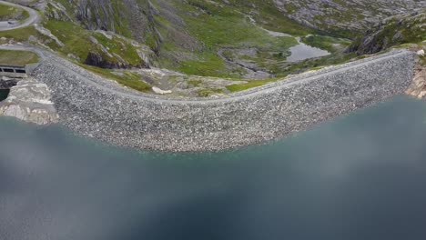 Tilting-down-on-a-man-made-pond-dam-with-blue-glacier-water-in-the-norwegian-mountains