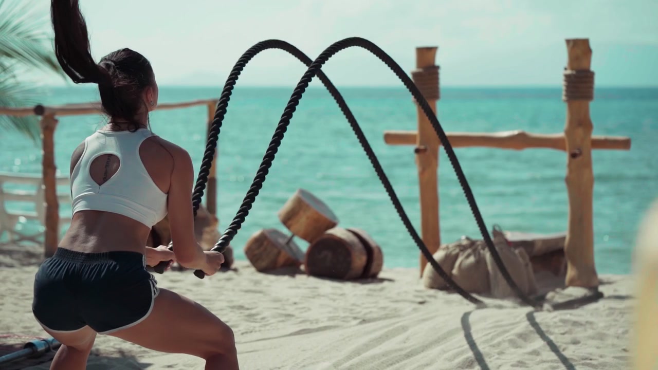 Fit Woman Exercising with Battle Ropes on Tropical Beach