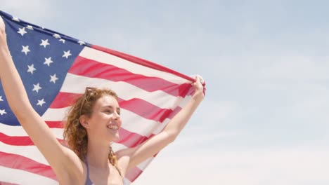 Seitenansicht-Einer-Kaukasischen-Frau-Mit-Wehender-Amerikanischer-Flagge,-Die-Am-Strand-Läuft-4k