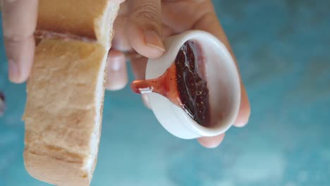 Hand pouring strawberry jam onto bread