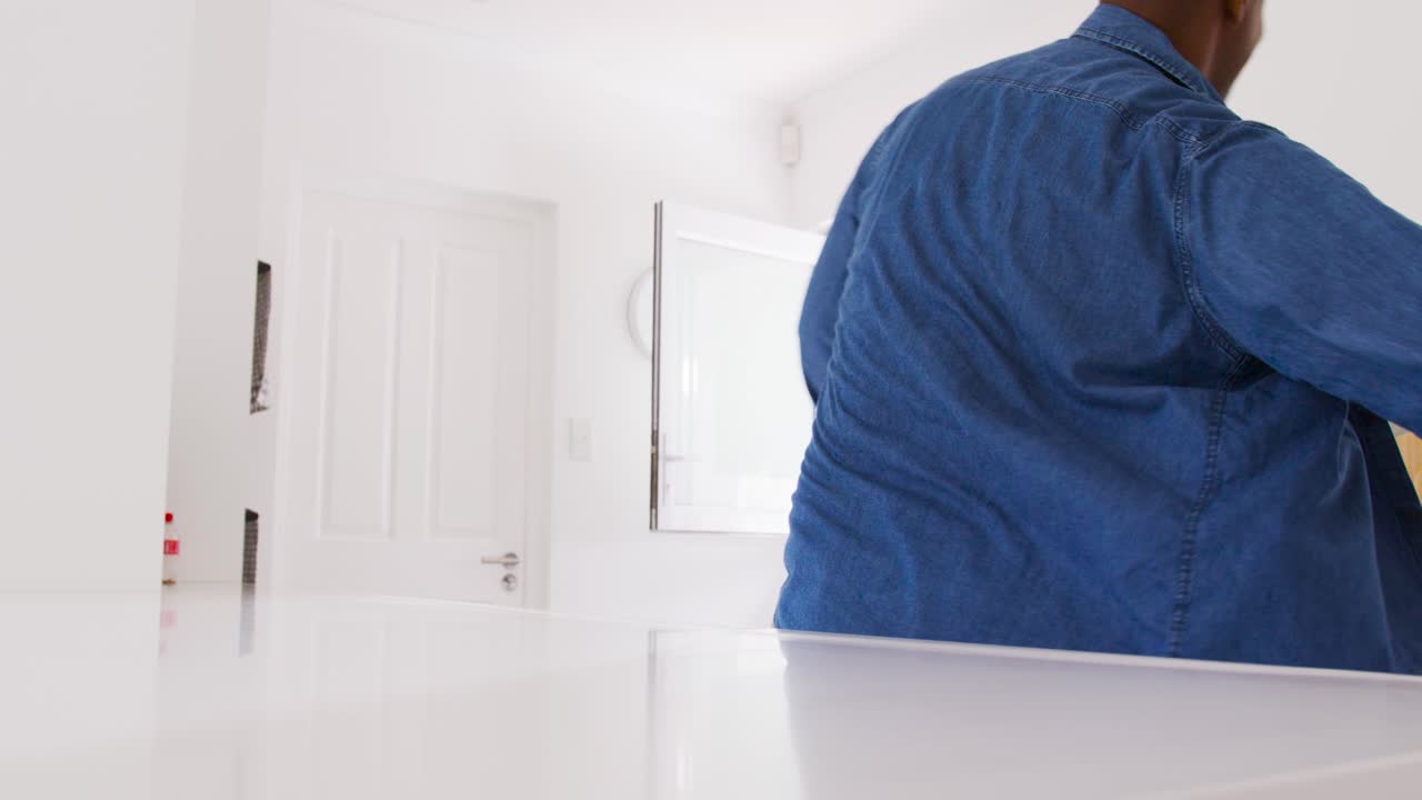 African American man grabbing cloth, using spray bottle, wiping white counter in kitchen, polishing