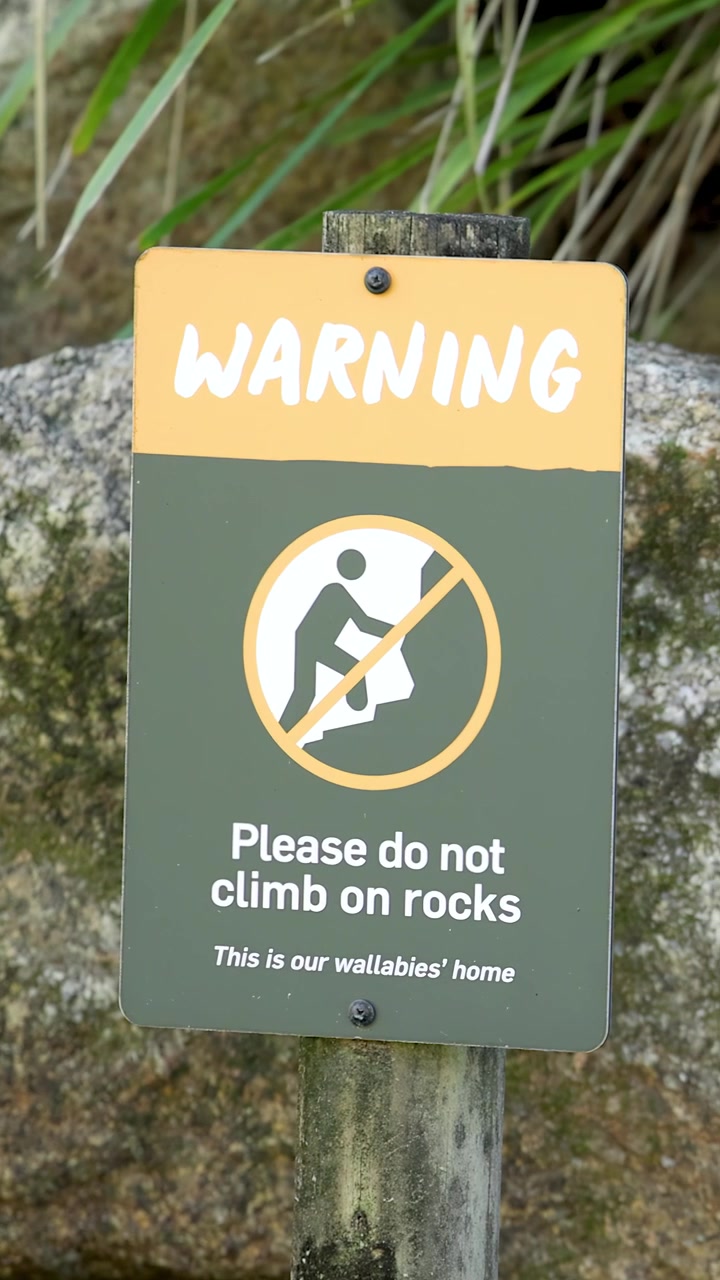 Close-up shot of a warning sign at a zoo with rocks and foliage background