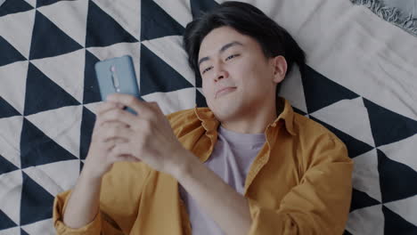 Young Man Relaxing in Bed and Using Smartphone